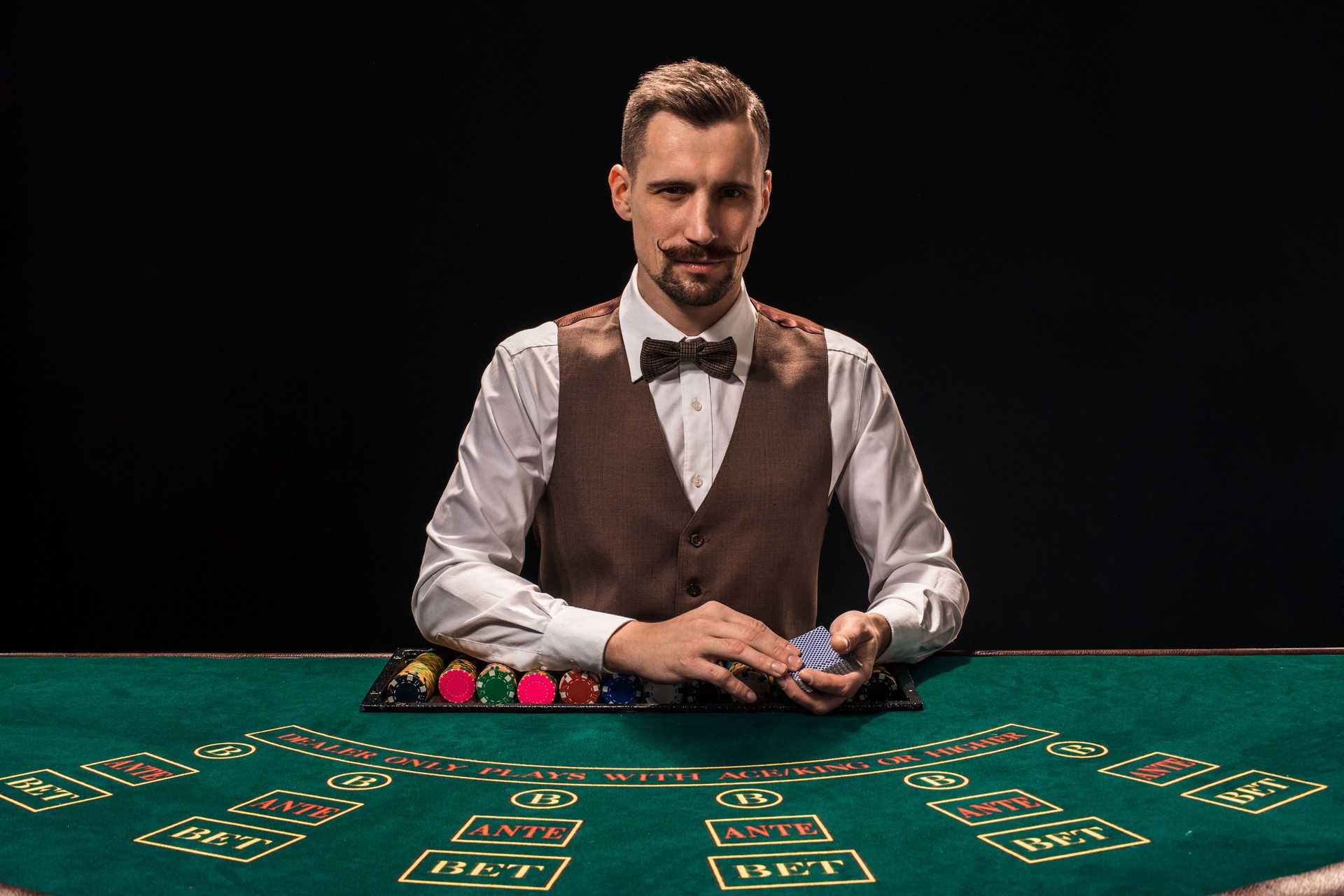 Portrait of a croupier is holding playing cards, gambling chips on table. Black background